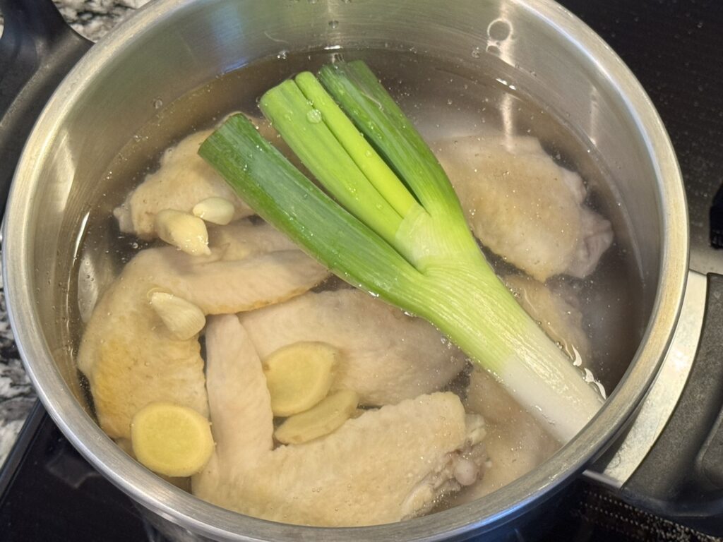 茹でた手羽先とネギとニンニクと生姜を圧力鍋に入れている様子