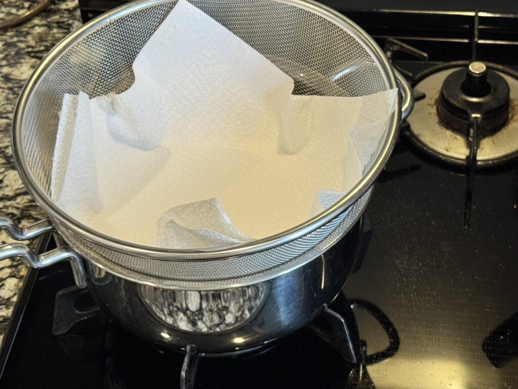 スープを濾すために鍋の上にザルを乗せてキッチンペーパーを置いている様子