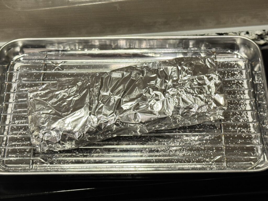 焼き上がってアルミホイルに包まれてバットの上に置かれているステーキ