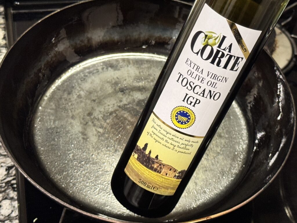 油を馴染ませた山田鉱業所の厚さ2.3mmの鉄フライパンに、オーケーストアのオリーブオイルを入れるところ