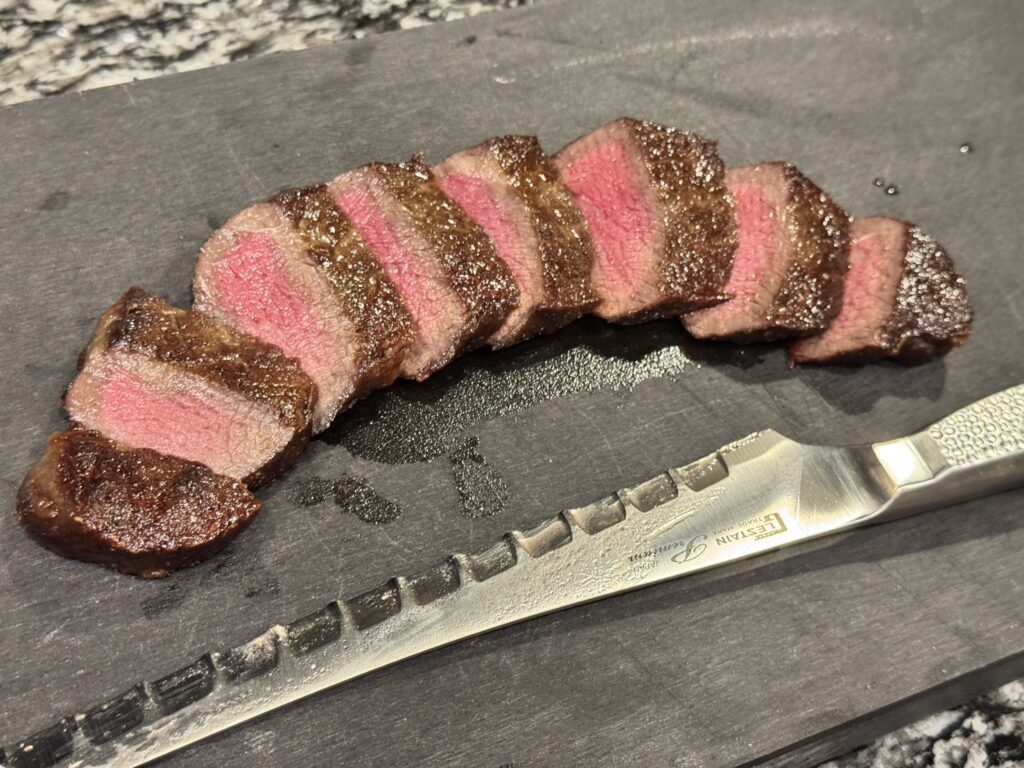 扇状に美しく並べられた牛ステーキのスライスとグレステンのスライスナイフ。完璧な焼き加減の断面が見えるおしゃれな盛り付け例。