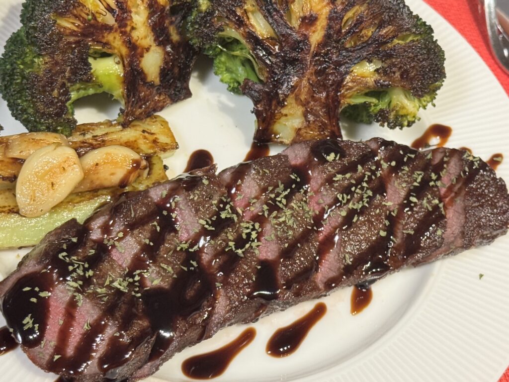 ミディアムレアに仕上げたステーキのワンプレート。ブロッコリーステーキとローストニンニクを添えた、彩り豊かなメインディッシュにバルサミコソースをかけた写真