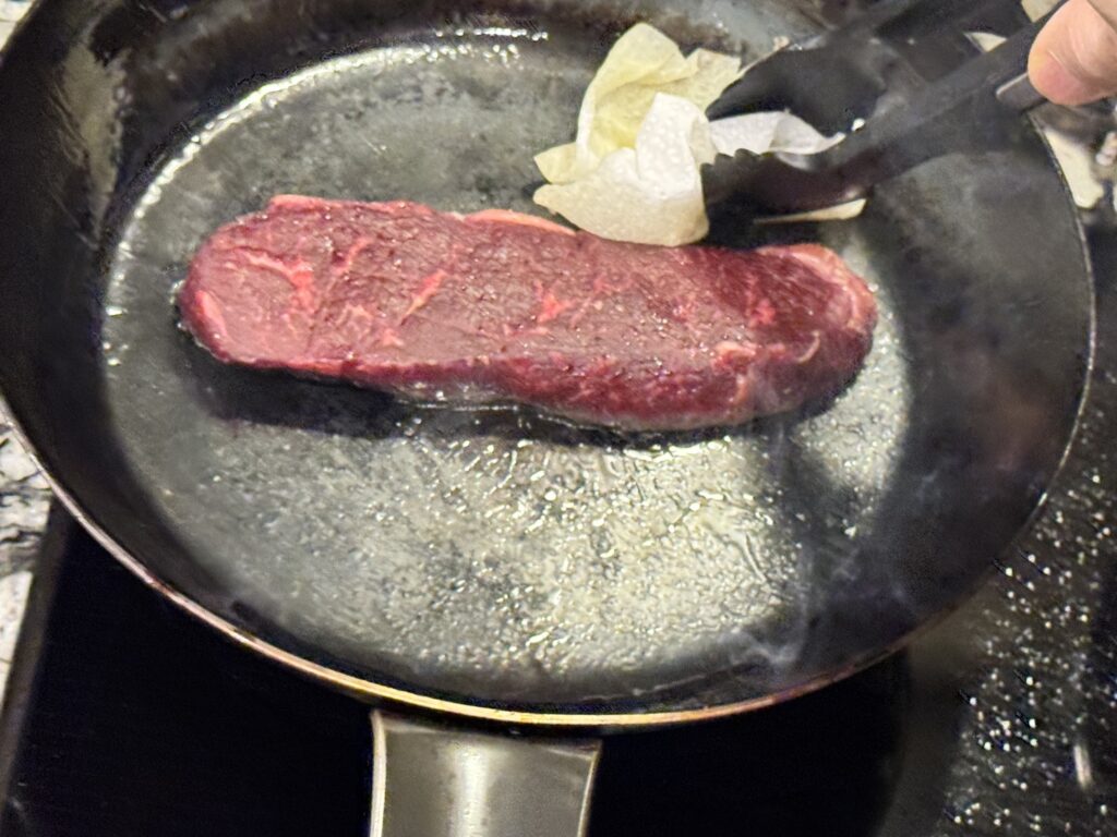 オーケーストアのオリーブオイルを入れた山田鉱業所の厚さ2.3mmの鉄フライパンにルビー色のオージービーフを焼いている写真