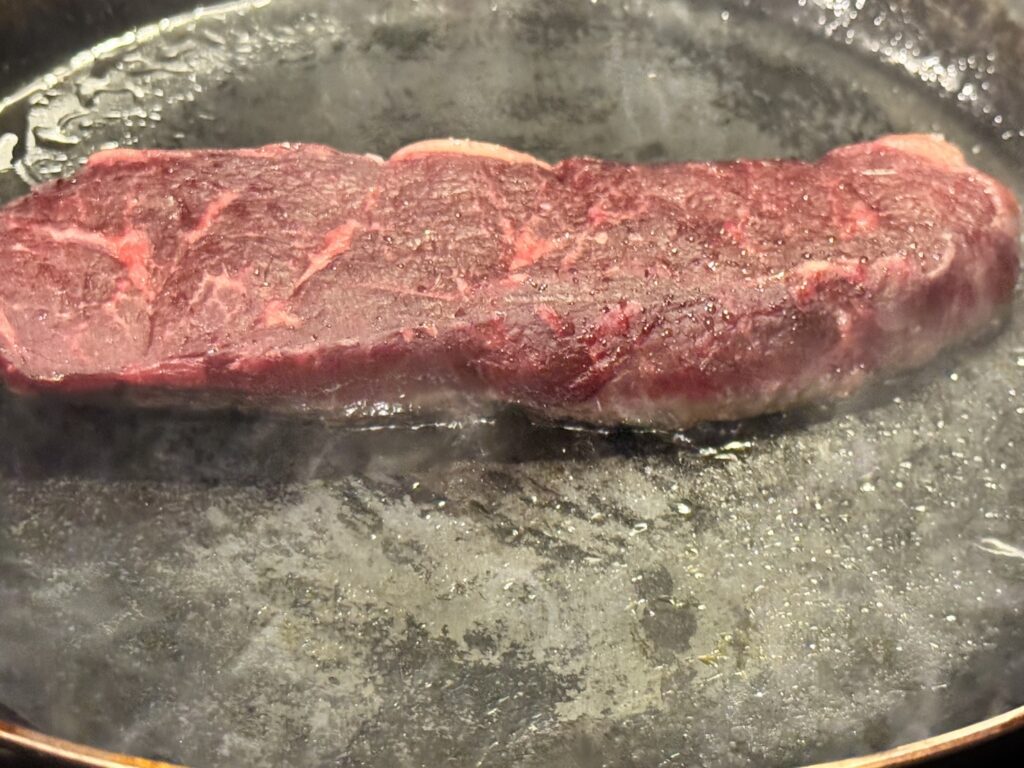 オーケーストアのオリーブオイルを入れた山田鉱業所の厚さ2.3mmの鉄フライパンにルビー色のオージービーフを焼いているアップ写真