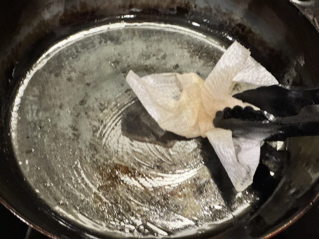 山田工業所の鉄フライパンでポークステーキを仕上げた後の油を拭いている様子