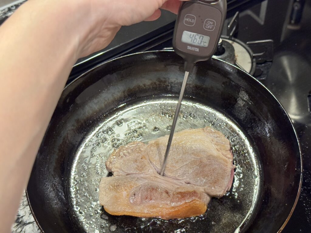 山田工業所の鉄フライパンで焼いている豚肉をタニタの温度計で中心温度を計測している様子